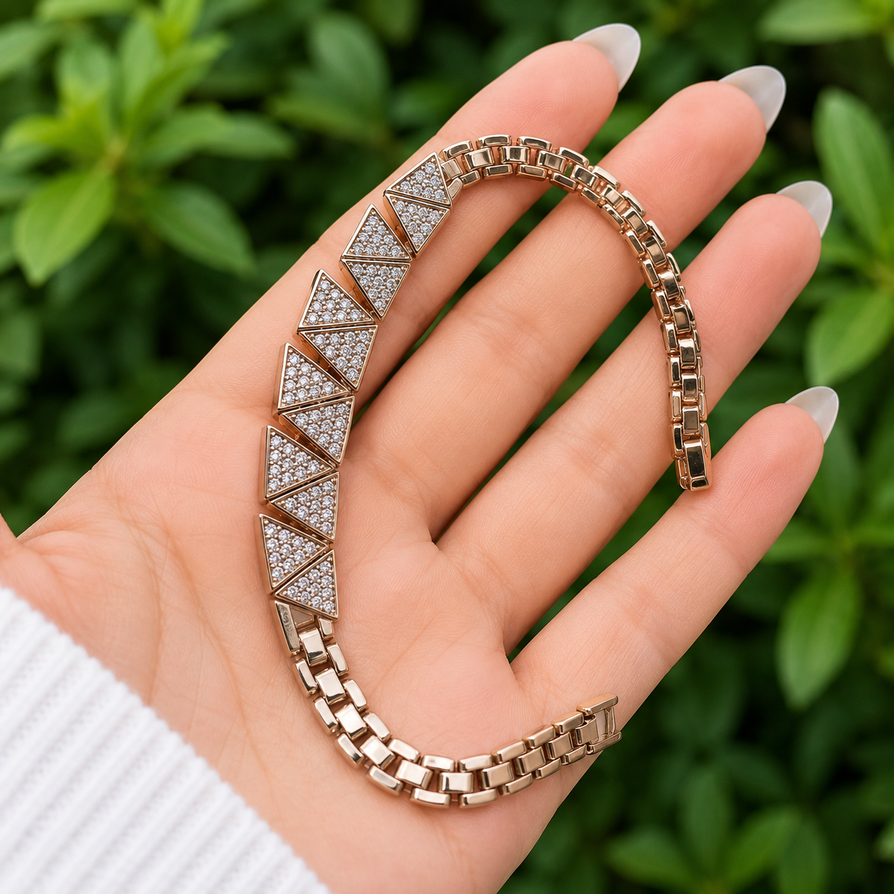 A rose gold chain bracelet with triangular pavé diamond sections, held in a hand against a blurred green foliage background.