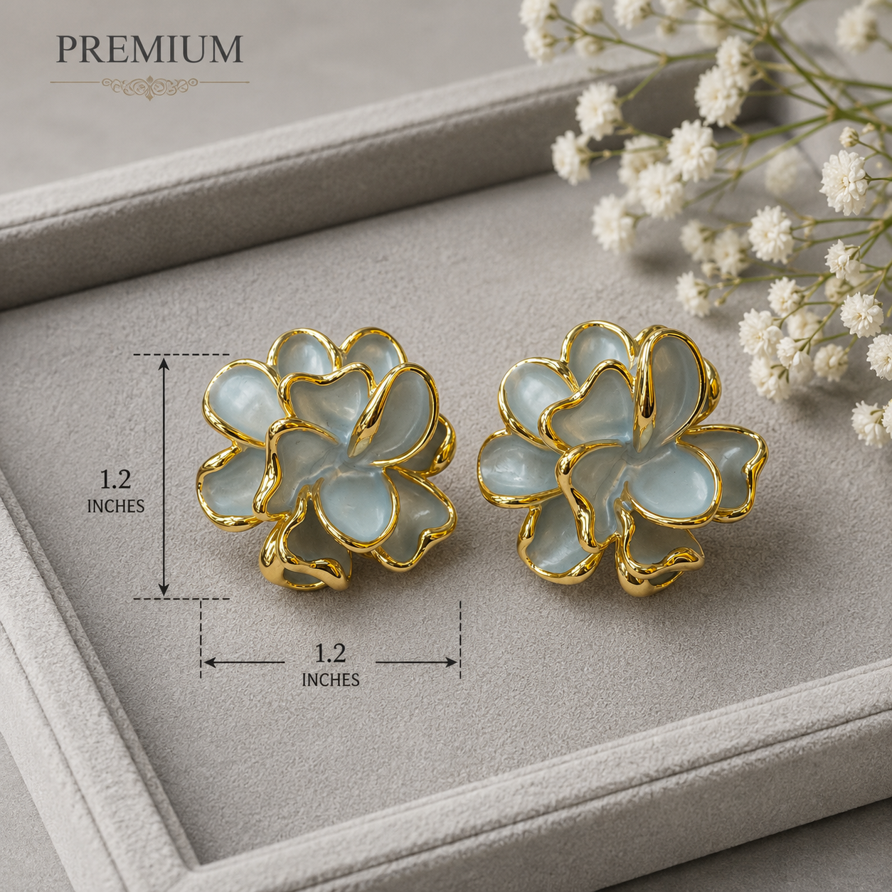 A pair of gold-tone flower-shaped stud earrings with pale blue-grey enamel petals, displayed on a gray jewelry tray with measurement annotations showing 1.2 inches on each side.