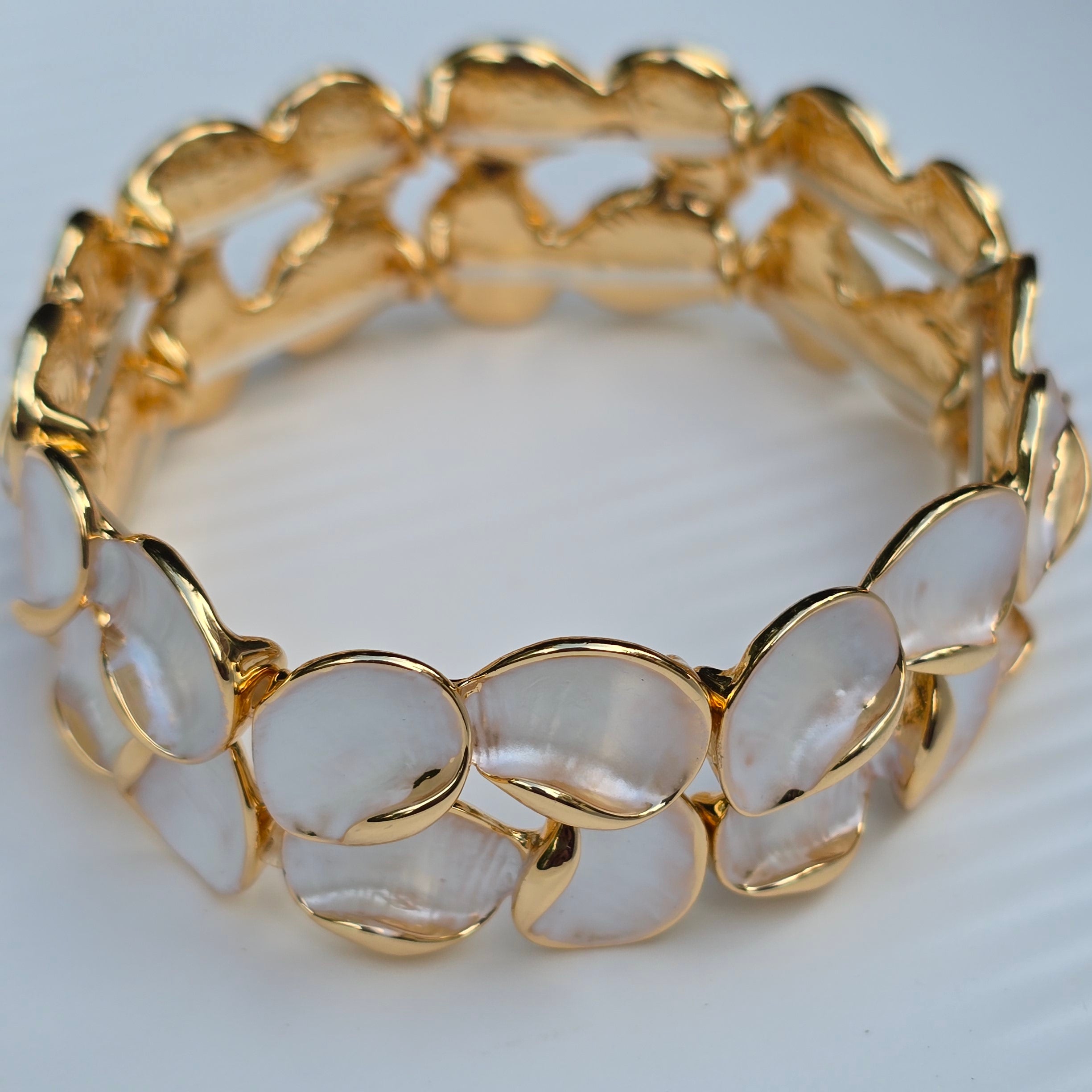 A gold-plated stretch bangle bracelet featuring smooth, oval, translucent white inlay stones, photographed on a light gray textured background.